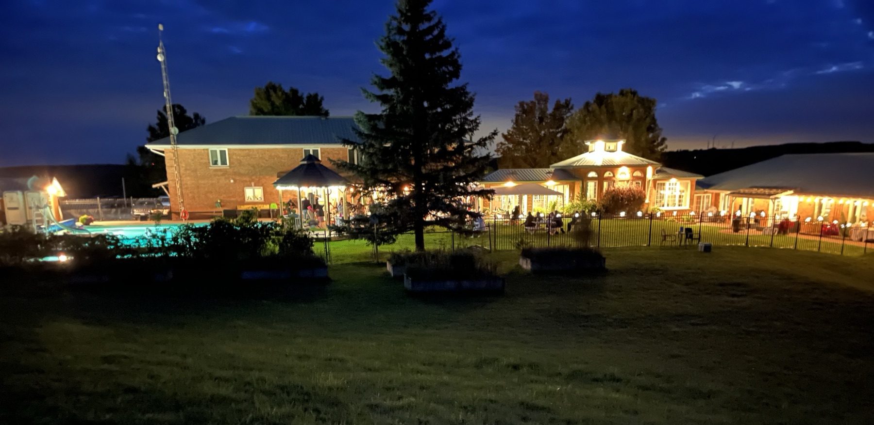 The property lit up at dusk with pool, gazebo, and house glowing
