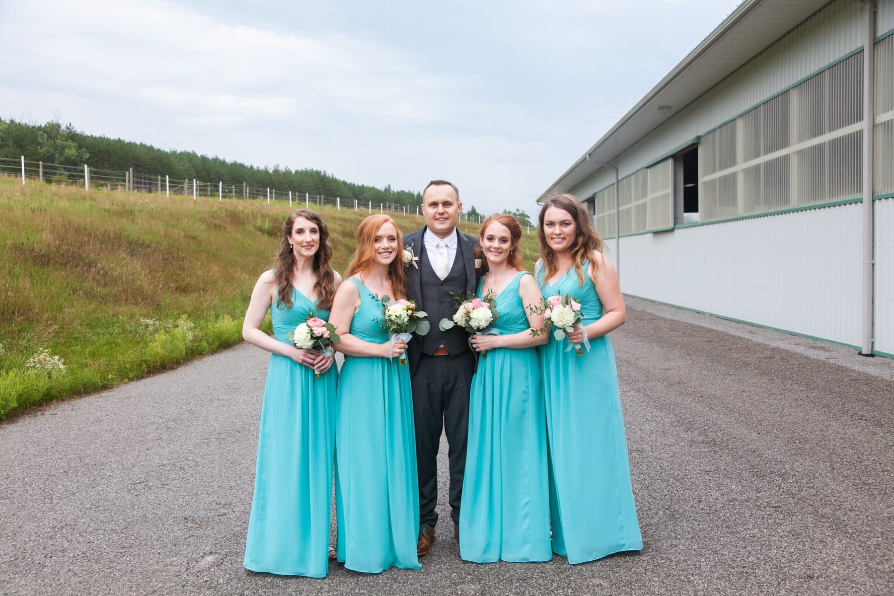 Bridesmaids and groom posed by the riding barn