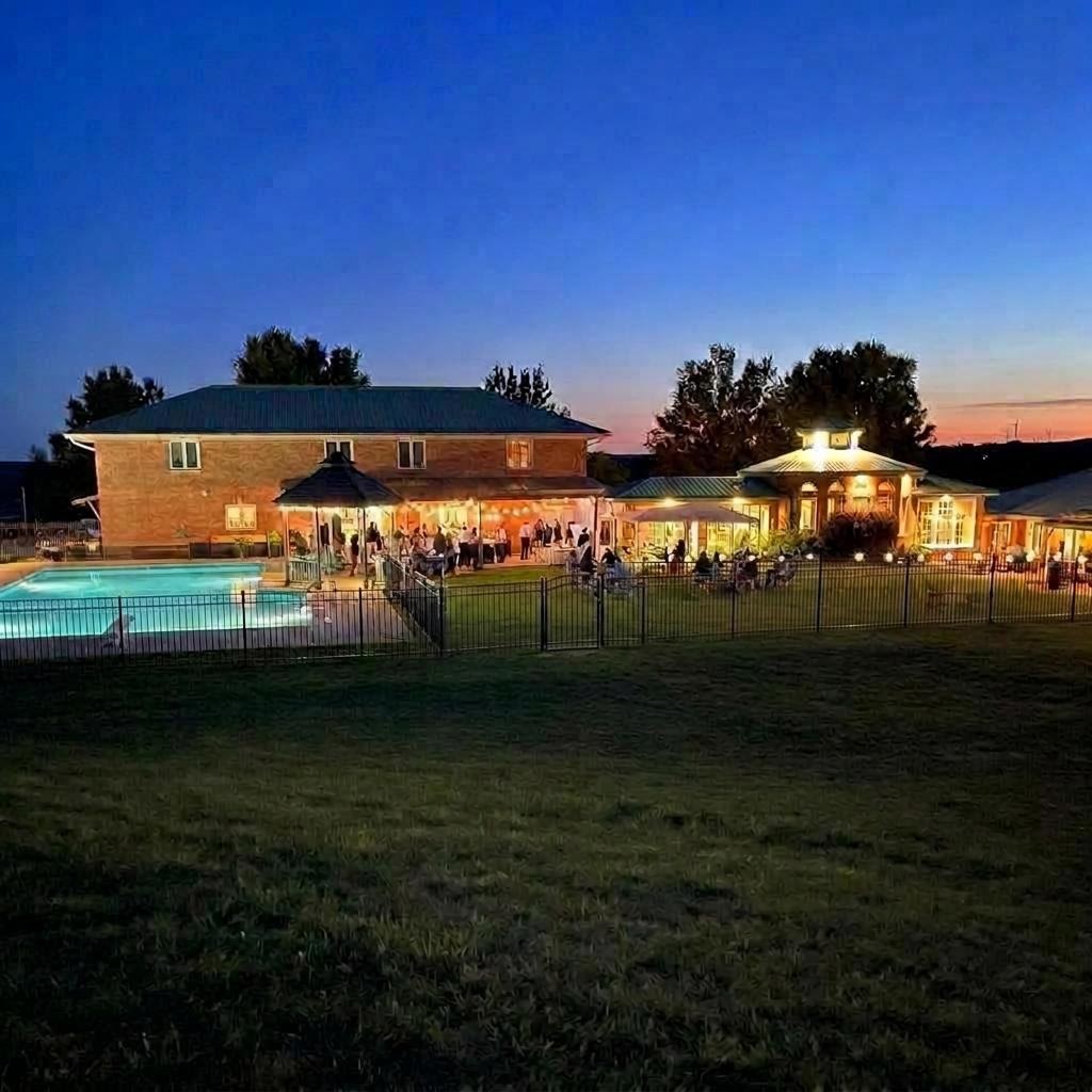 The property lit up at dusk with the pool, gazebo, house, and reception spaces glowing